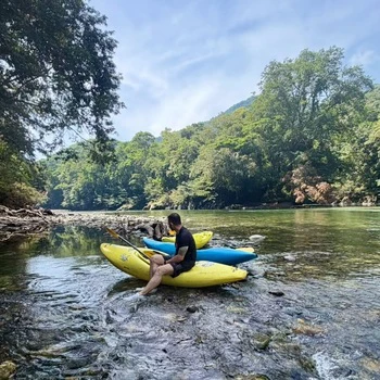 1 kayaker sat on a yellow kayak, with 3 kayaks on the beach and the Samaná River in the background during the kayak course