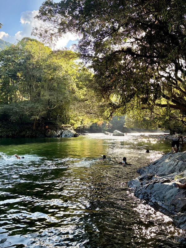 Four people swimming in La Poseta pool on the Santo Domingo River, Colombia, at sunset.