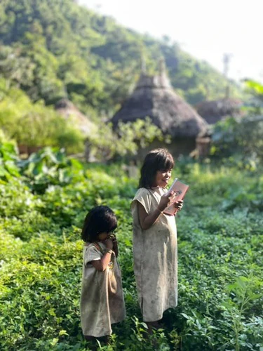 Two indigenous children with a book in hand in front of their traditional homes.