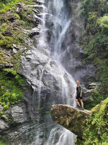 Woman standing on a rock in front of La Esmeralda Waterfall in the Waterfall Valley, Antioquia